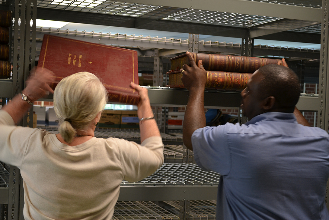 two people take historical records off a shelf